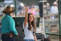 a woman in a cowboy hat waves to the crowd at a rodeo