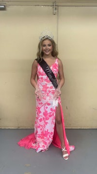 a woman in a pink dress holding a sash